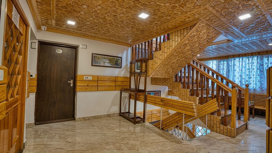 Staircase area at Royal Comfort Regency featuring wooden steps, handrails and ceiling panels with framed photographs on the walls.