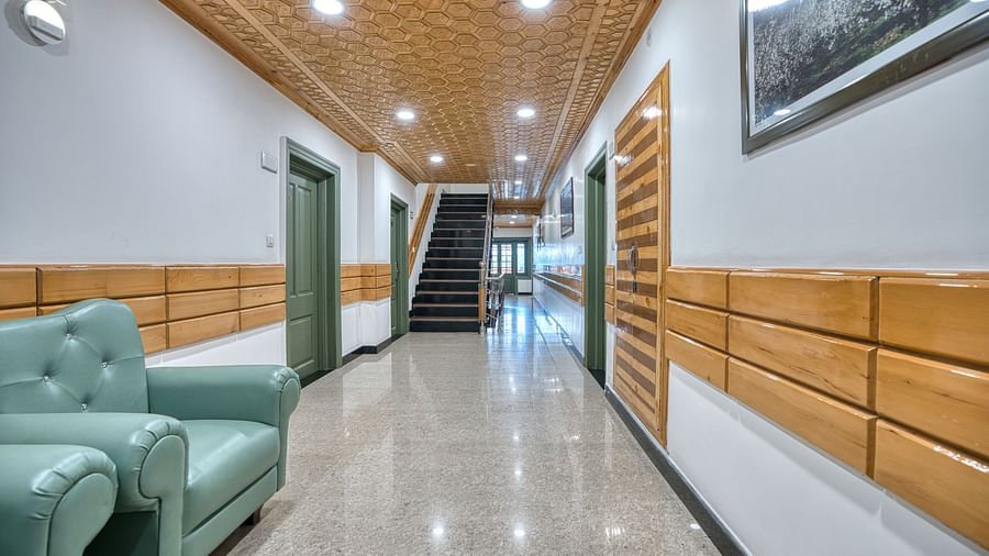 A hallway at Royal Comfort Regency with green seating, wooden wall panelling and framed artwork leading towards a staircase in the background.