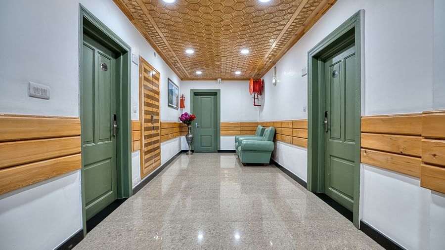 A well-lit hallway inside Royal Comfort Regency with marble flooring, wooden panelling and a green sofa placed against the wall.