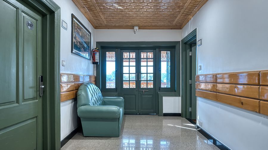 A narrow seating area at Royal Comfort Regency with green armchairs, wooden wall detailing and a large window letting in daylight.