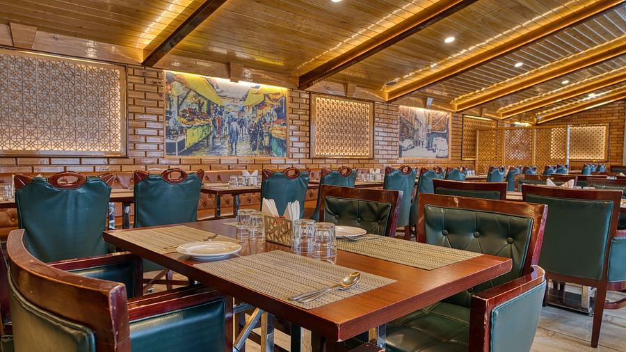 Well-lit dining area with wooden interiors and green chairs at Royal Comfort Regency, offering a warm and inviting restaurant setting.
