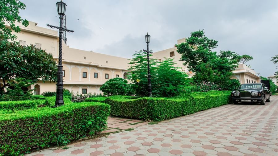 A stone pathway bordered by green hedges and lamp posts, leading to the entrance of Royal Heritage Haveli.