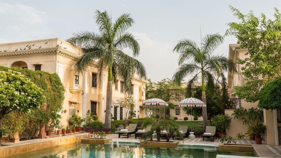 A swimming pool area surrounded by palm trees and buildings at Royal Heritage Haveli.