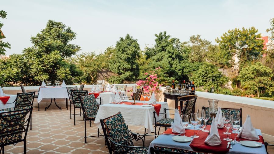 An outdoor dining terrace at Royal Heritage Haveli with tables set, overlooking trees and a distant landscape.