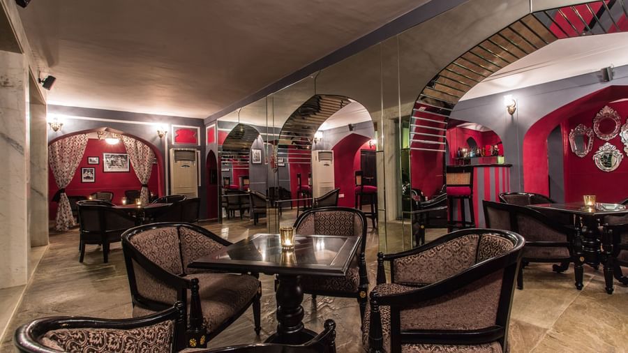Interior view of a restaurant or bar area at Royal Heritage Haveli with red accents, arched doorways, and wooden tables and chairs.