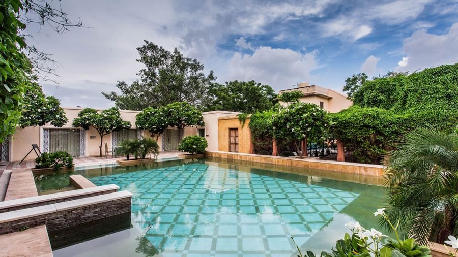 A view of a swimming pool with a building and lush greenery under a partly cloudy sky.