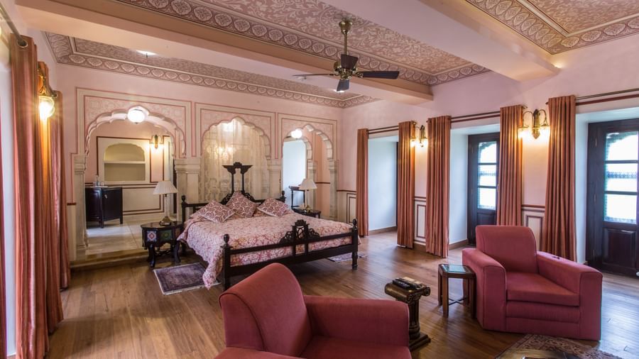 A spacious living area of a suite at Royal Heritage Haveli with traditional furniture, a ceiling fan, and light-coloured walls.