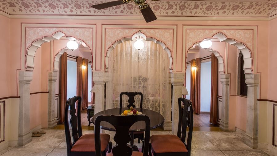 An indoor dining or sitting room at Royal Heritage Haveli with a wooden table and chairs, set against intricately designed walls and arched doorways.