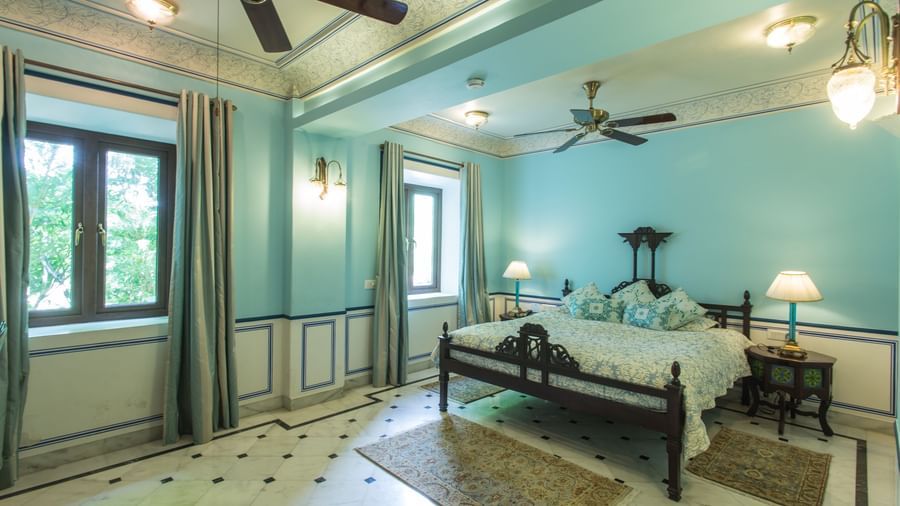 A spacious bedroom at Royal Heritage Haveli with a bed, seating area, ceiling fans, and light blue walls.