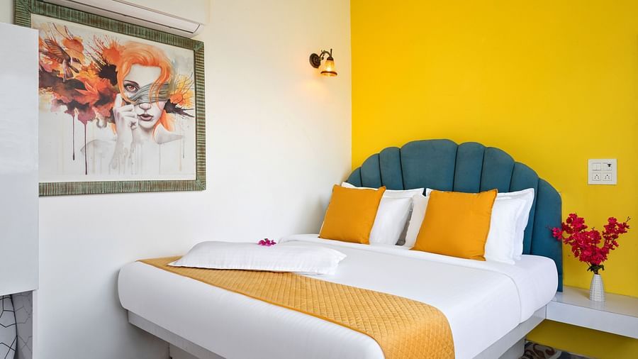 A bright bedroom with a teal headboard, colourful linens, and a large window offering a scenic view.