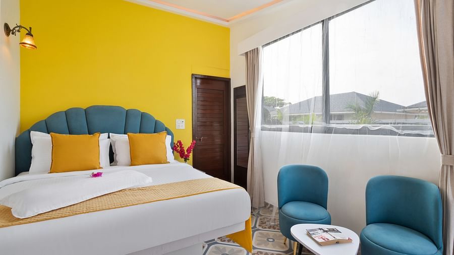 A bright, modern bedroom, a large window, a cosy double bed, and teal armchairs.