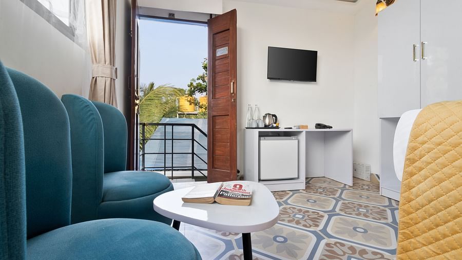 A compact sitting area with teal chairs, a round table, and an open door revealing an outdoor view.
