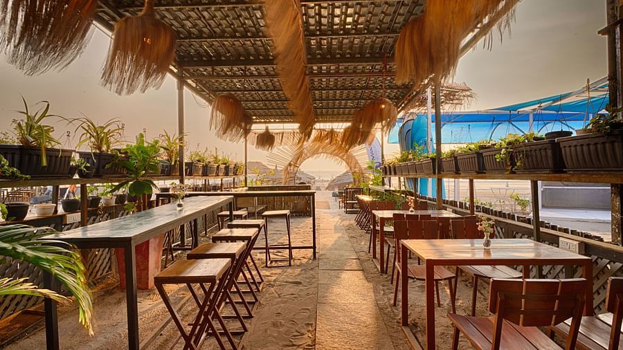 A restaurant with thatched roofs and wooden tables, overlooking the beach.