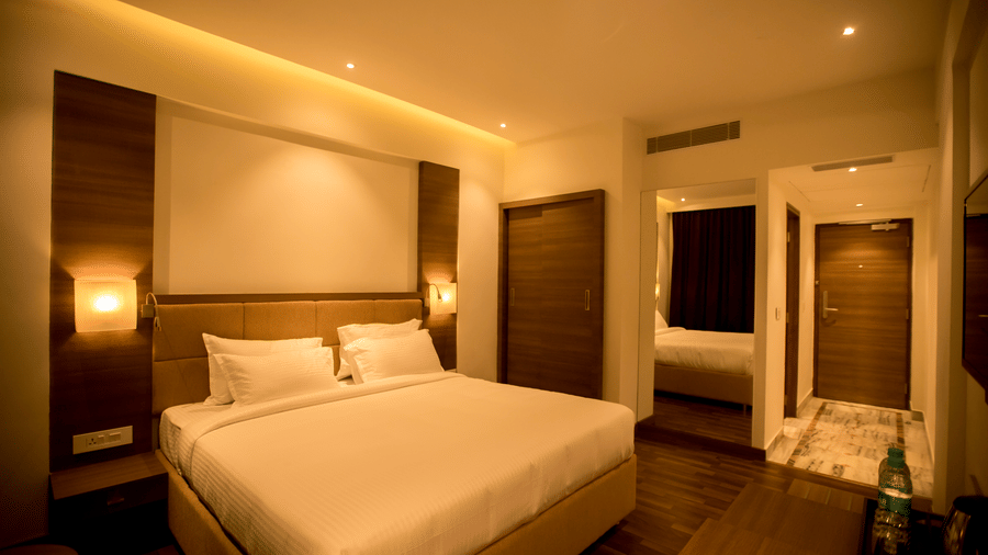 A brightly lit hotel bedroom has a king size bed and a full length mirror visible near the side of the room at S Hotels, Chennai.
