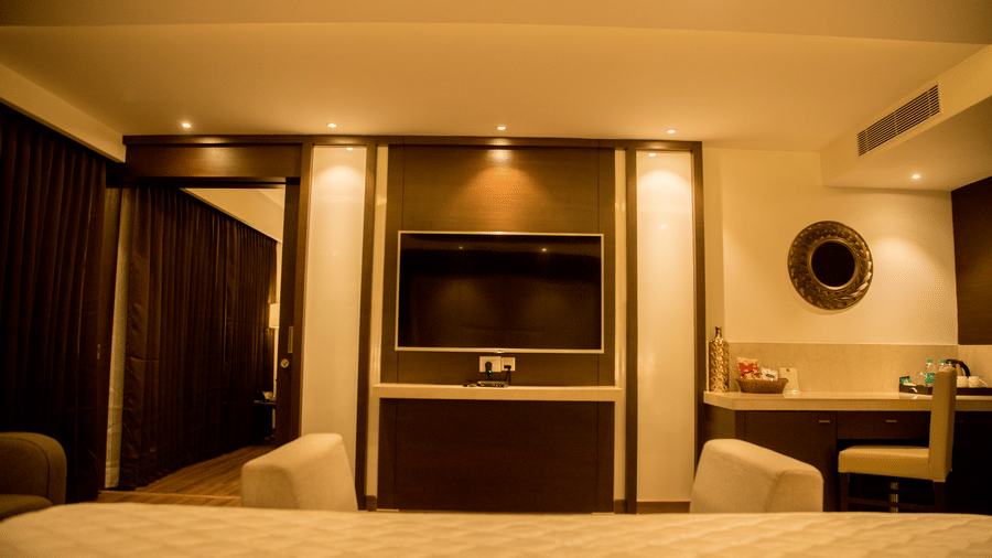 A hotel room with a neatly made king size bed also features a small dressing table and a circular mirror on the wall at S Hotels, Chennai