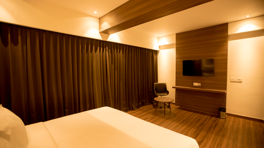 A corner view of a hotel bedroom shows a king size bed and a wall-mounted television at S Hotels, Chennai.