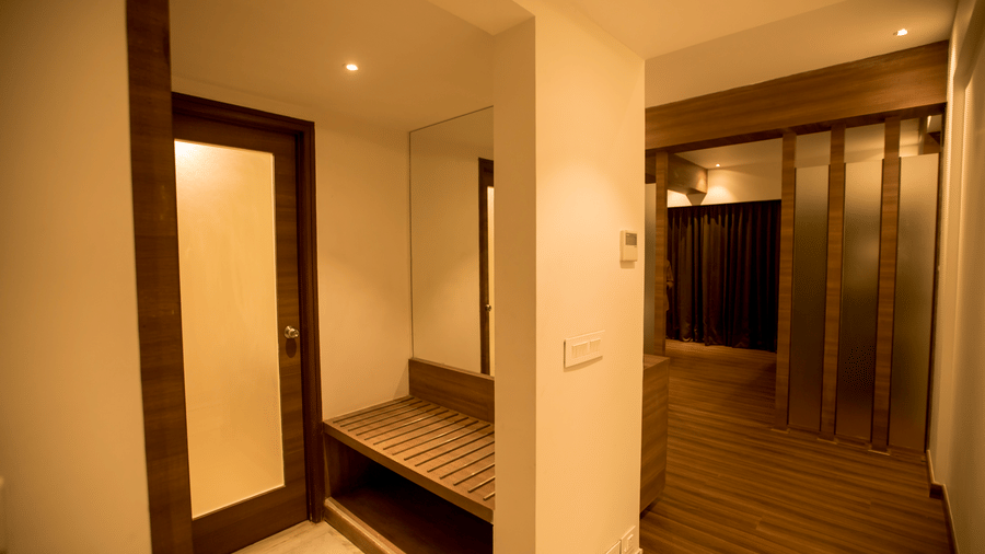A hotel room view shows a wooden storage bench in a short corridor leading into the main bedroom area at S Hotels, Chennai.