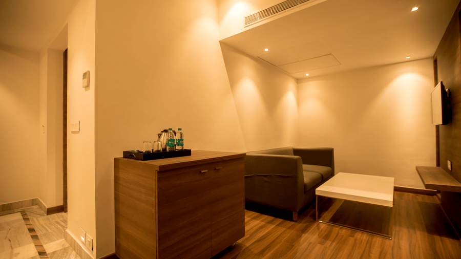 A hotel suite living area features a dark sofa, a wooden cabinet, and recessed ceiling lighting at S Hotels, Chennai.