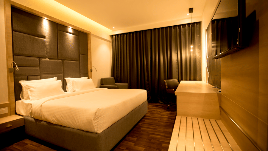 A modern hotel bedroom features a king size bed with a cushioned headboard and wooden flooring at S Hotels, Chennai.