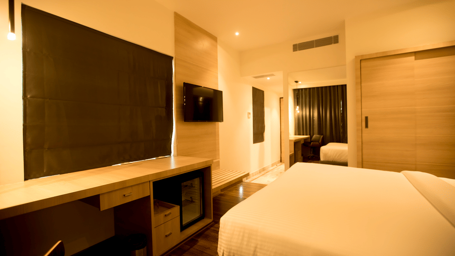 A compact hotel room shows a neatly made king size bed and a wall mounted television opposite the sleeping area at S Hotels, Chennai.