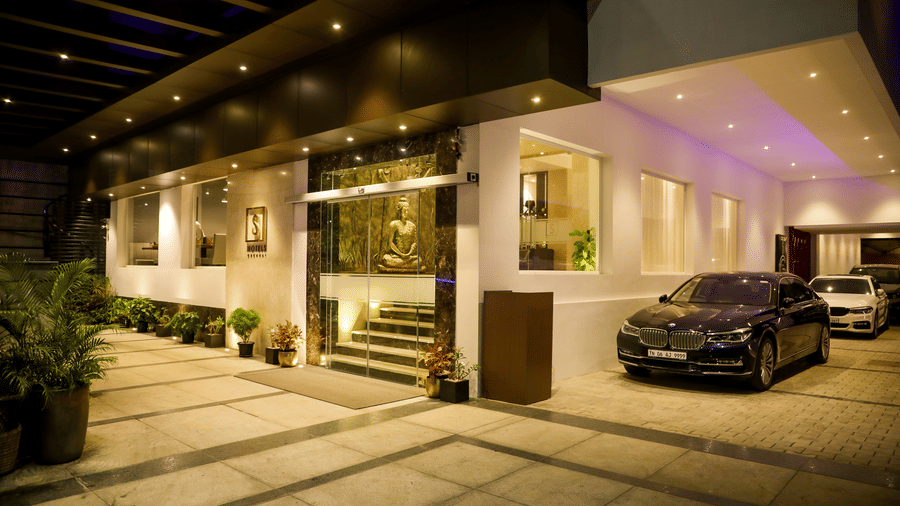 The exterior of a hotel entrance is visible at night with a parked black car and bright lighting illuminating the drive at S Hotels, Chennai.