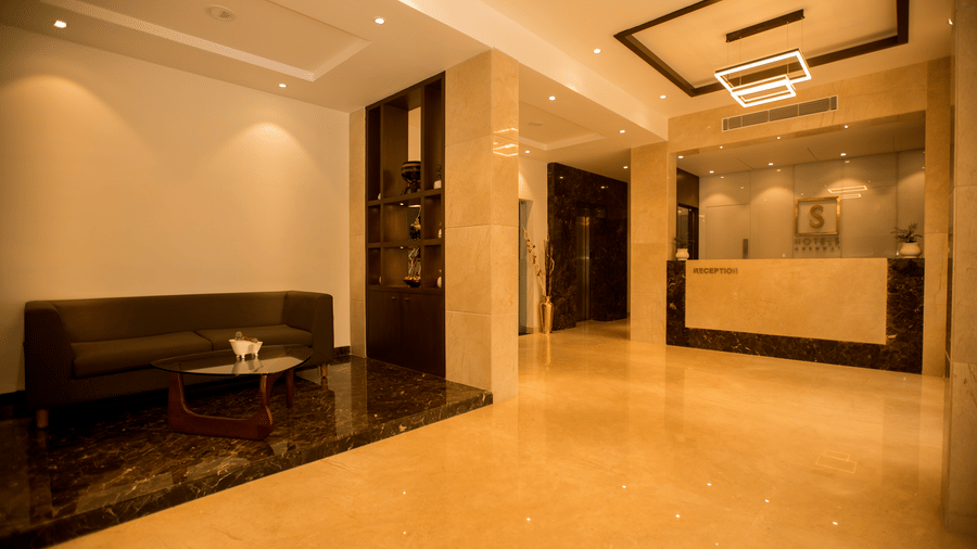 A hotel reception and lobby area features polished marble floors a low sofa and a brightly lit check in desk in the background at S Hotels, Chennai.