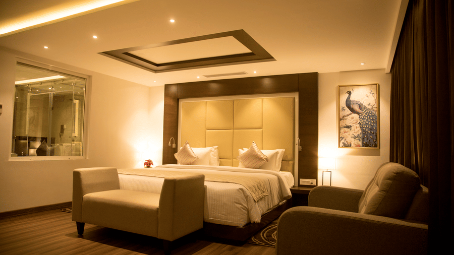 A modern hotel bedroom features a king size bed with soft lighting and an upholstere bed bench at the foot of the bed in the foreground at S Hotels, Chennai