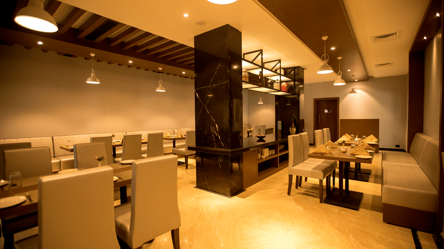 A blurred view of a modern fine-dining restaurant shows several empty tables with chairs and dim lighting at S Hotels, Chennai.