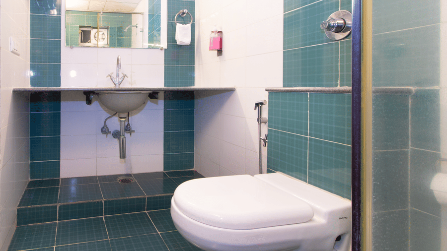 Bathroom with teal mosaic tiles, a wall-mounted sink, and a toilet at Sanctum Suites Indiranagar, Bangalore.
