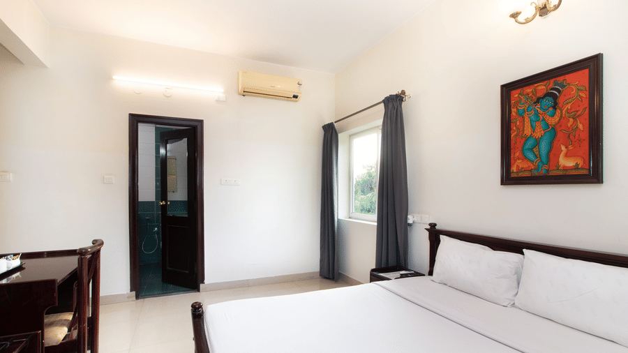 Bright and airy hotel room with a double bed, an air conditioner, and traditional wall art at Sanctum Suites Indiranagar, Bangalore.
