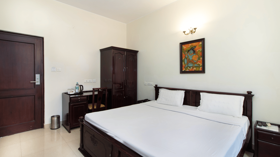 Hotel room with a double bed, a dark wooden wardrobe, and a window with natural light at Sanctum Suites Indiranagar, Bangalore.