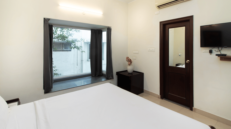 Hotel room with a double bed, wooden furniture, a television, and a wooden door at Sanctum Suites Indiranagar, Bangalore.