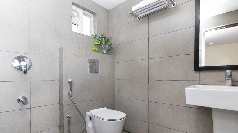 A bathroom at Sanctum Suites, Richmond Road, Bangalore features a toilet, a white washbasin, and a mirror.
