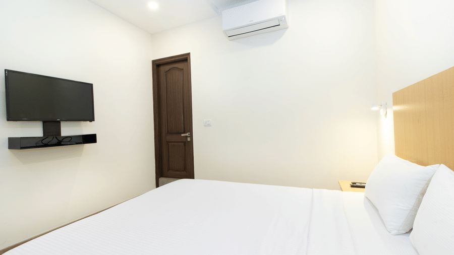 A room at Sanctum Suites, Richmond Road, Bangalore features a double bed with white linens, a wall mounted television, and  A/C.