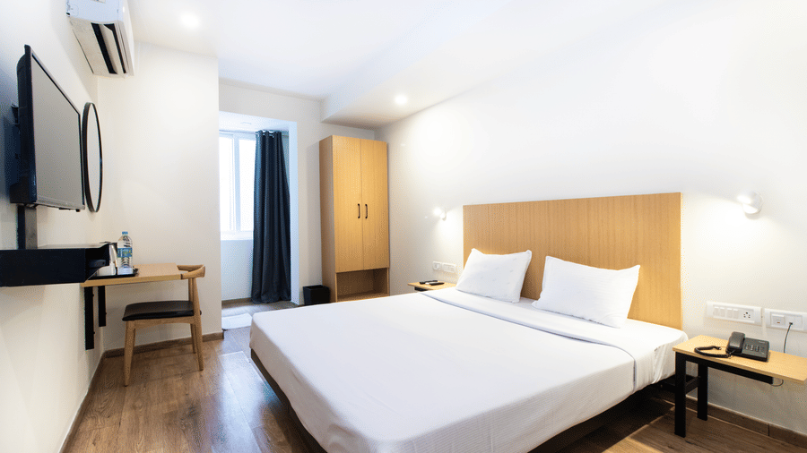 A bedroom at Sanctum Suites, Richmond Road, Bangalore features a large bed, a dressing table, a wardrobe, a wall mounted television and A/C.