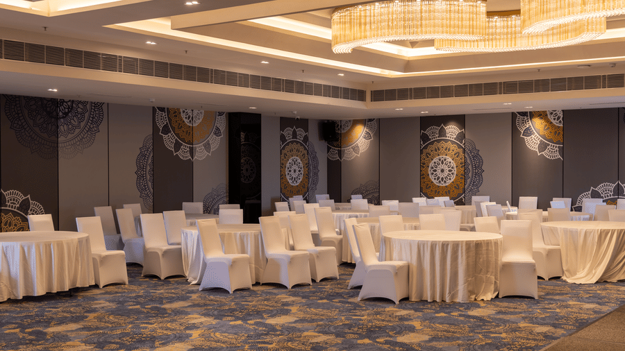 Elegant banquet venue showing a patterned blue carpet and 1 crystal chandelier at Sands Point Hotel, Pondicherry.