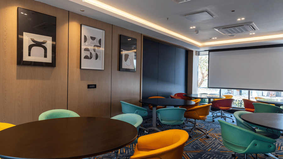 Vibrant meeting space with 1 large projector screen and colourful chairs at Sands Point Hotel, Pondicherry.