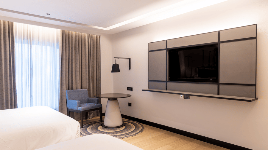The Family Room at Sands Point Hotel, Pondicherry, featuring a large flat-screen television mounted on the white wall, a round dark table with a white conical pedestal base.