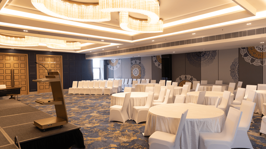 Spacious ballroom arranged with 5 round tables and white chair covers at Sands Point Hotel, Pondicherry.