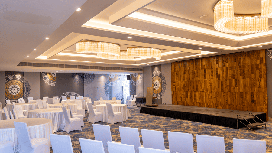 Large event space with a wooden stage and 2 tiers of recessed ceiling lights at Sands Point Hotel, Pondicherry.