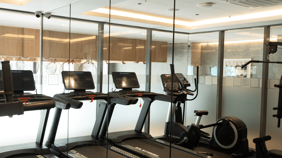 A bright workout area with 1 stationary bike and multiple cardio machines at Sands Point Hotel, Pondicherry.
