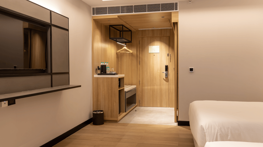 An entry-way and amenities corner of the Sands Point Hotel, Pondicherry, Premium Twin Room featuring a wooden wardrobe with clothes hangers, a tea and coffee station with water bottles and glasses on a white counter-top.