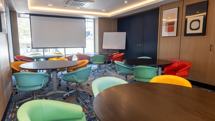 A modern waiting area with 4 upholstered chairs and a glass partition at Sands Point Hotel, Pondicherry.