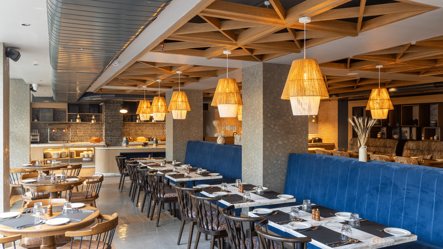 Long dining tables and 1 blue velvet banquette under woven pendant lights at Sands Point Hotel, Pondicherry.