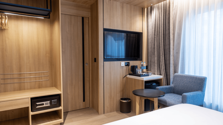 A Standard Room at Sands Point Hotel, Pondicherry,  featuring a wooden wardrobe with clothes hangers, a digital safe,a television. 
