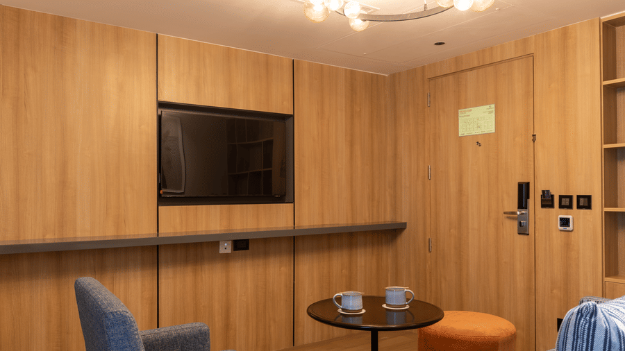 Wood-panelled walls featuring a wall-mounted TV and 1 blue chair at Sands Point Hotel, Pondicherry.