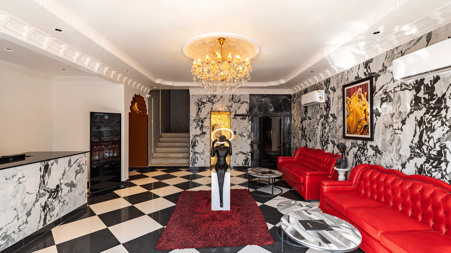 Luxury hotel lobby with a black and white chequered floor, red velvet seating, and a large chandelier.