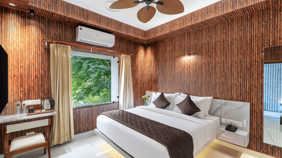 Boutique hotel room featuring a king-size bed, timber cladding, a wicker ceiling fan, and a large window overlooking lush greenery.