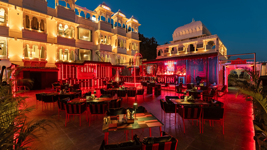 Exterior night shot of a white heritage hotel building with a patio bar and seating lit dramatically in bright red.