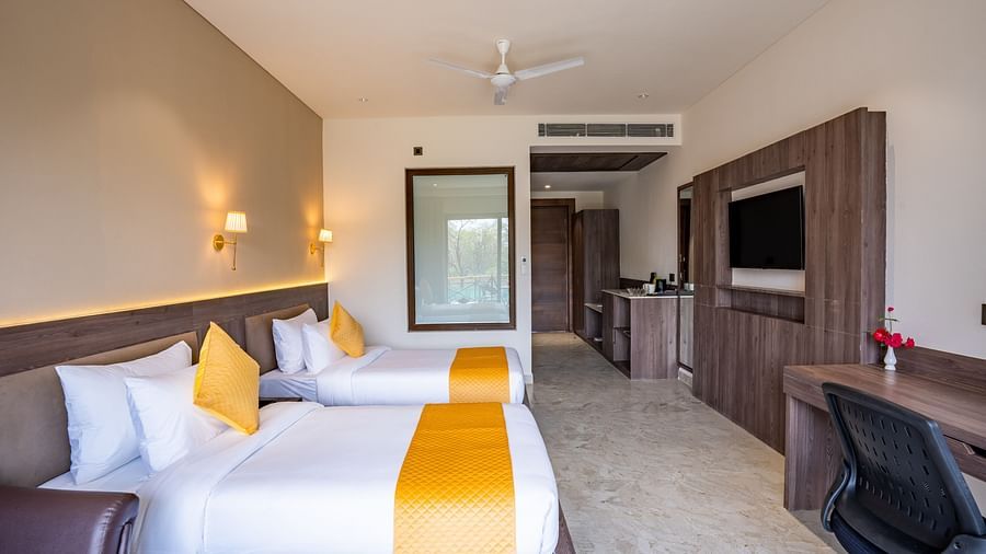 A hotel room with a large bed with orange pillows placed in front of a wall mounted television - Shervani Pebbles & Pines, Corbett